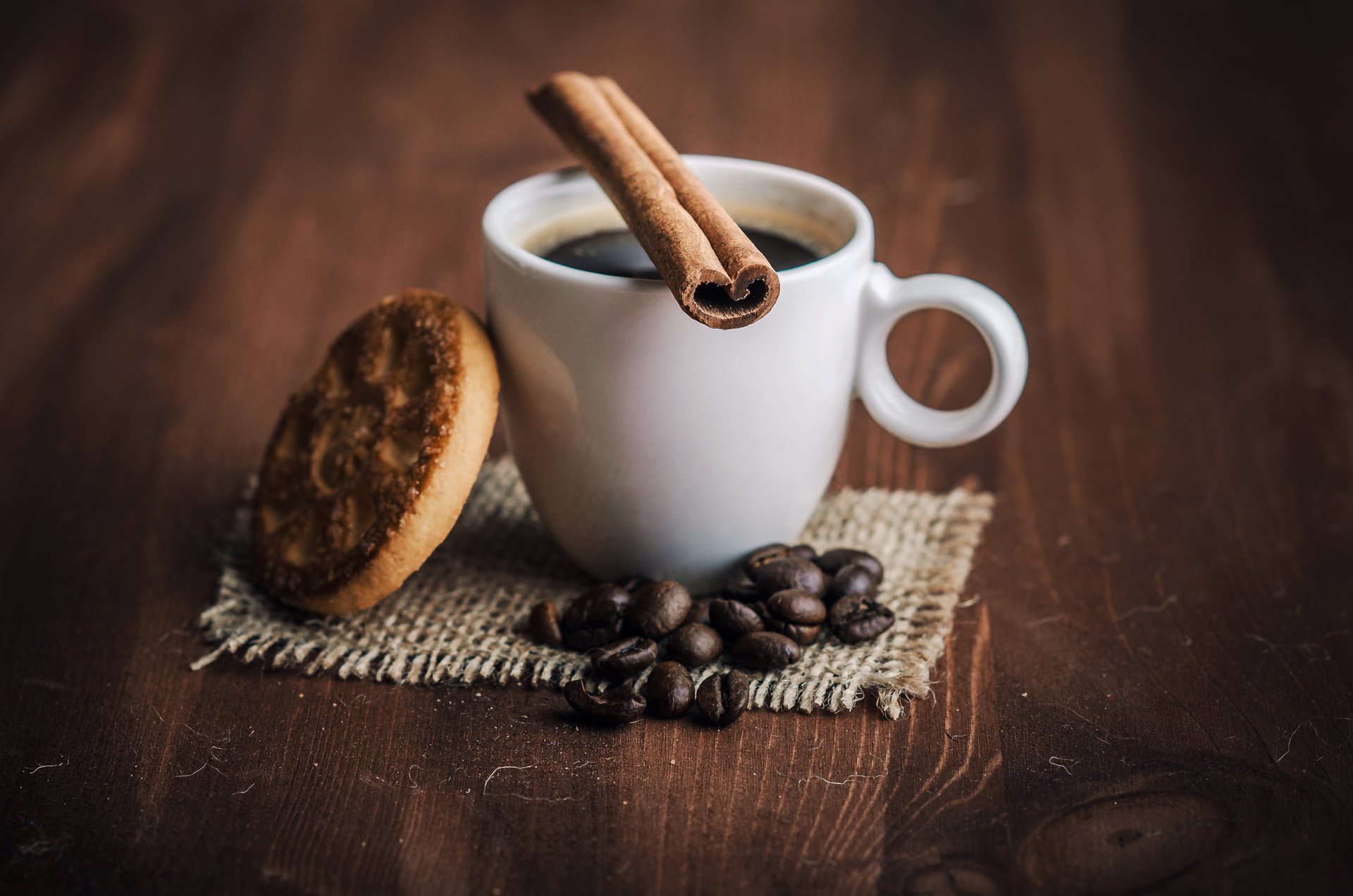 On the wooden table is a white cup with coffee, cinnamon, liver and coffee beans